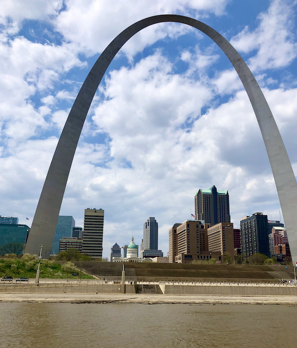 The huge metal Gateway Arch Saint Louis MO with buildings and muddy river.