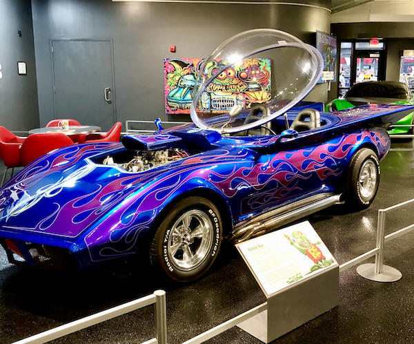 A royal purple corvette with a glass bubble roof that's open.