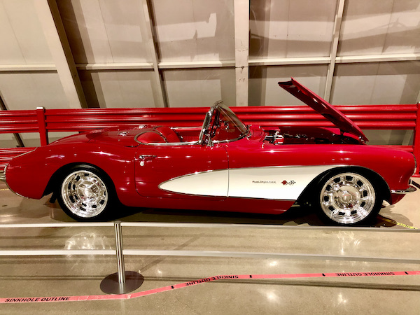 A red Corvette convertible with white scoop and hood up at the National Corvette Museum
