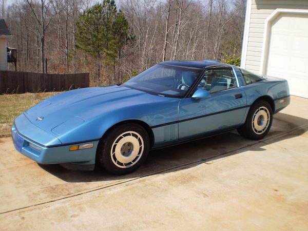 A medium metallic blue 1987 Corvette in a driveway.
