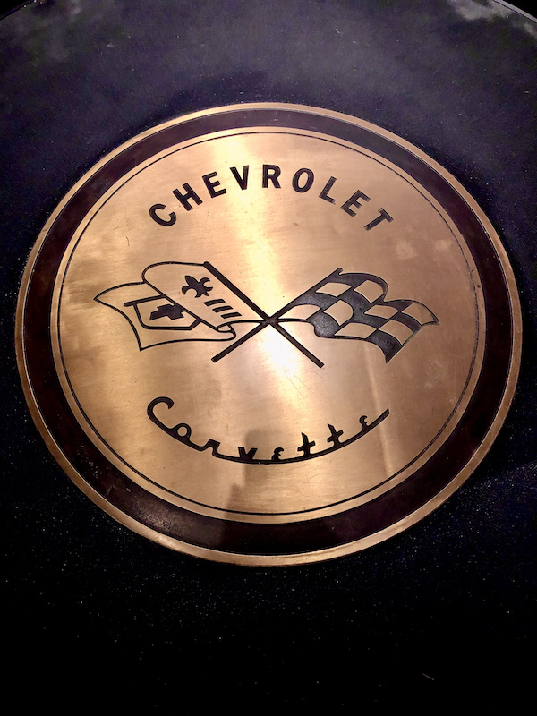A gold insignia with black checkered flag crossed with a fleur d lis flag.