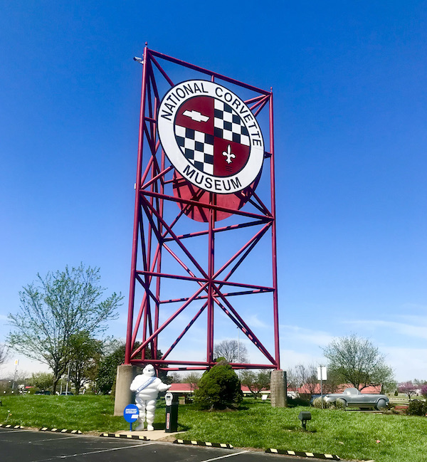 A large red steel sign against a blue sky announcing you're at the National Corvette Museum.