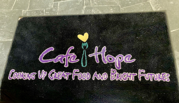 A black welcome mat with purple writing at Café Hope Gretna Louisiana