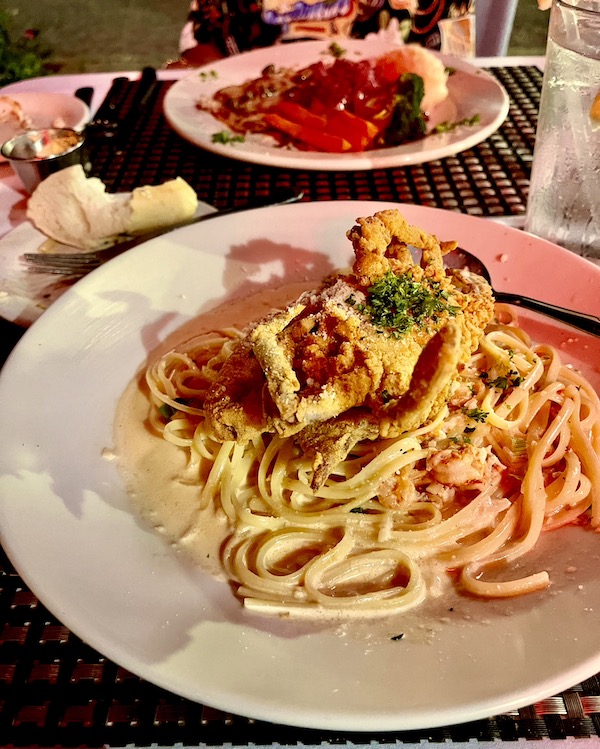 A white plate topped with pasta mixed with crawfish tail meat and a fried crab at Maple Street Café New Orleans