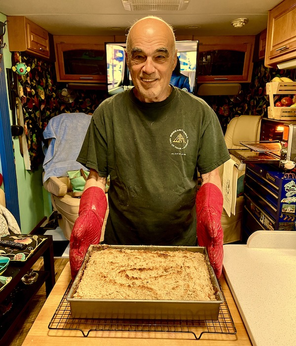 A man with red oven mitts holding a baking pan filled with cake.