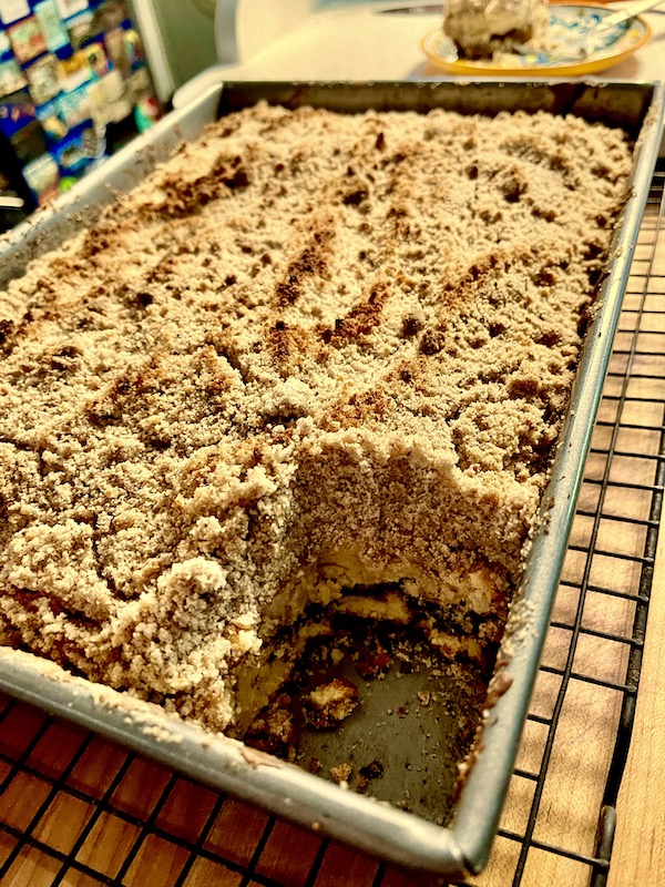 A rectangular baking pan filled with coffee cake and a piece removed from the corner.