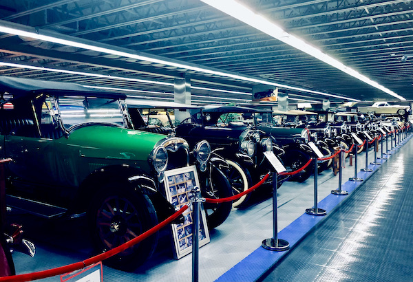A row of antique convertibles. All but the first one are black. The first is green.