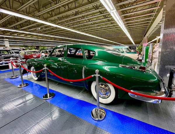 An emerald green antique car with wide white wall tires.