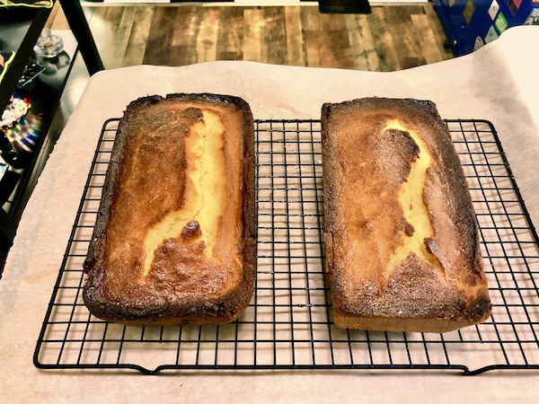 A pair of A Taste of Sunshine Lemon Cakes out of the pan sitting on a black wire rack.