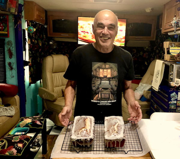 A man in a black Tee shirt presenting two loaf cakes with glaze in our RV kitchen.