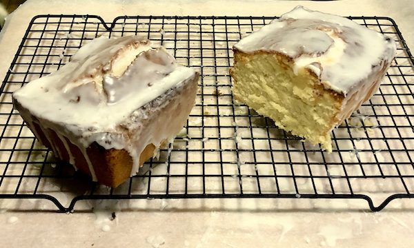 A glazed loaf cake is cut in half to reveal the moist crumb.