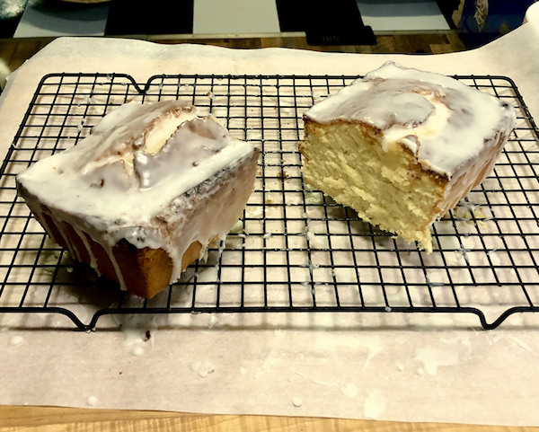 A glazed loaf cake is cut in half to reveal the moist crumb.
