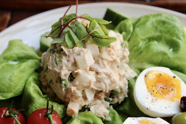 A large plate of food that includes a mound of tuna salad, lettuce, tomato and halved hard boiled eggs from Just a Few Miles South