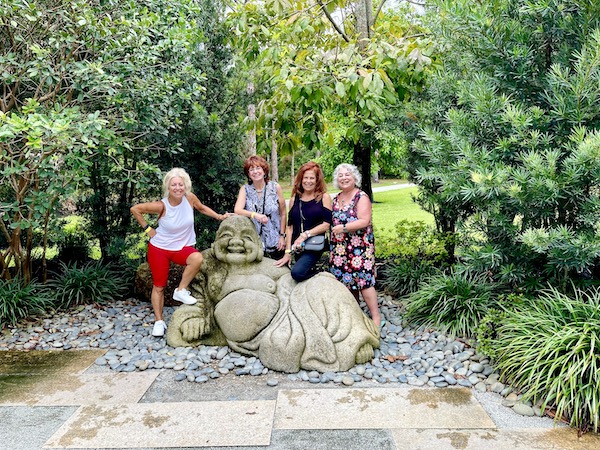 A smiling buddha sculpture with 4 women standing behind it at Morikami Museum and Japanese Gardens