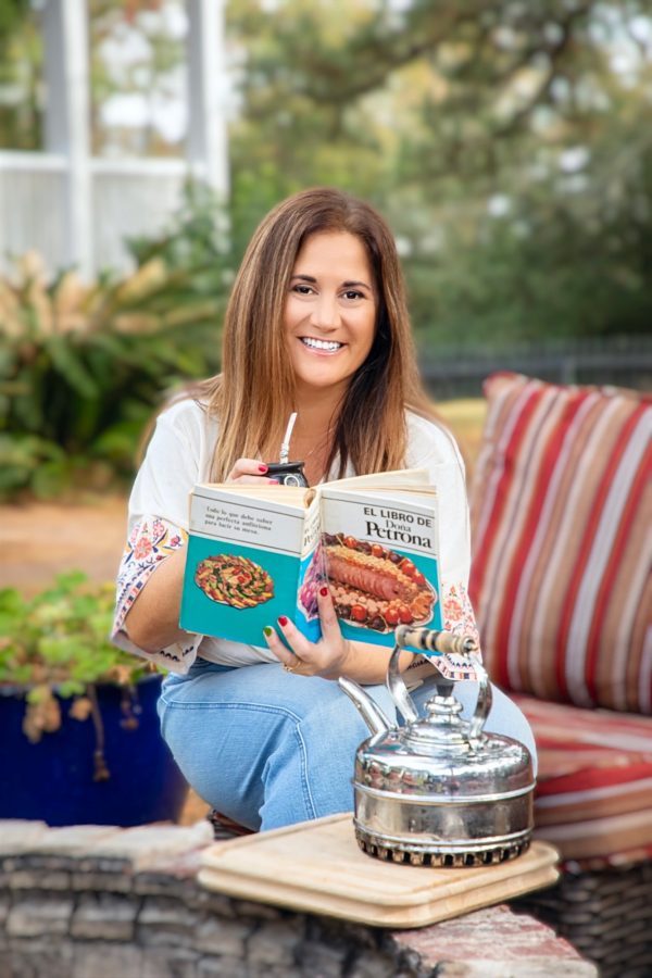 A young woman sitting on a patio chair reading a book.