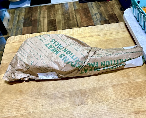 A butcher paper wrapped steak on a wood cutting board.