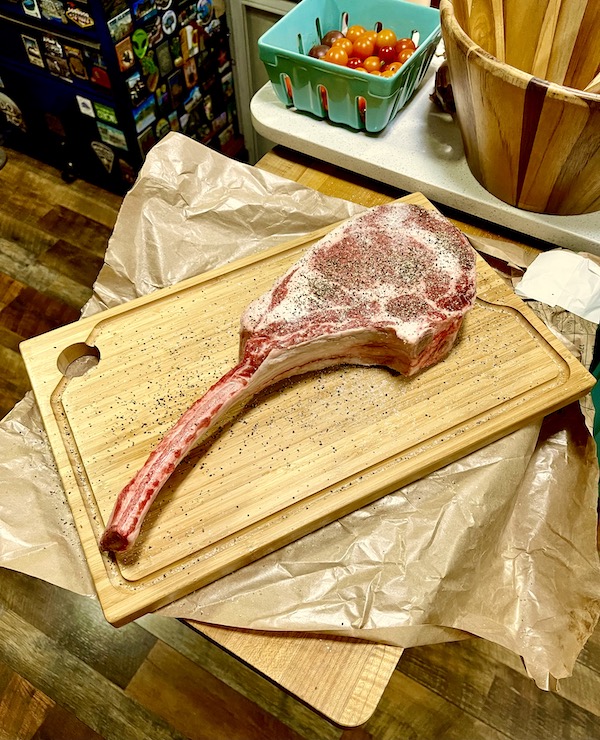 A well seasoned bone in steak on a cutting board for Tomahawk Steak on the Grill