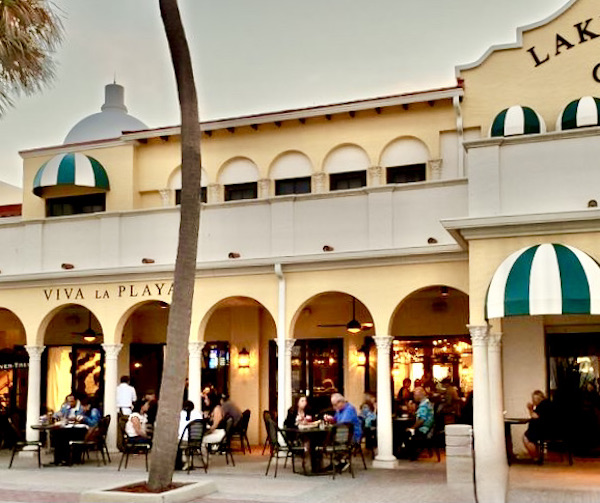 A yellow Spanish style two story building with arches and tables and chairs.