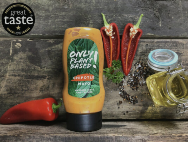 A bottle of orange colored mayo with red peppers on a wood table