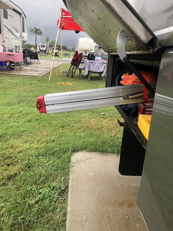 A closed folding ladder partway out of an RV storage bay.