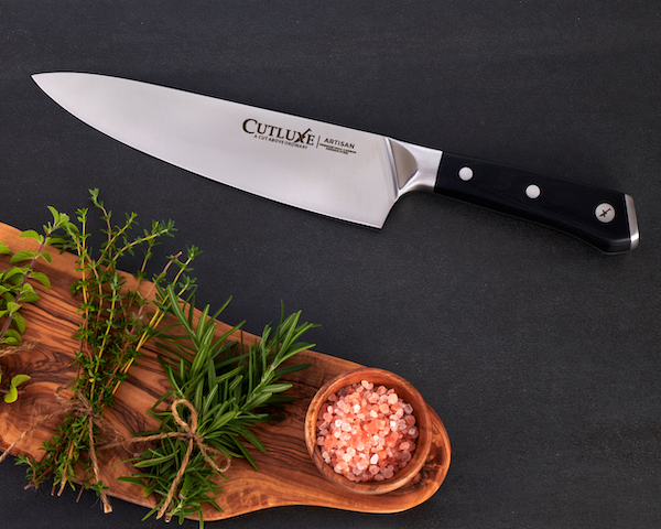 A chef knife on a dark wood surface with herb sprigs from 15 Best Gifts for Foodies and RVers
