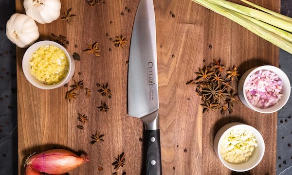 A wood cutting board with a chef knife, shallots, onion and assorted items from15 Best Gifts for Foodies and RVers