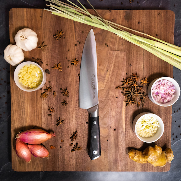 A wood cutting board with a chef knife, shallots, onion and assorted items from15 Best Gifts for Foodies and RVers