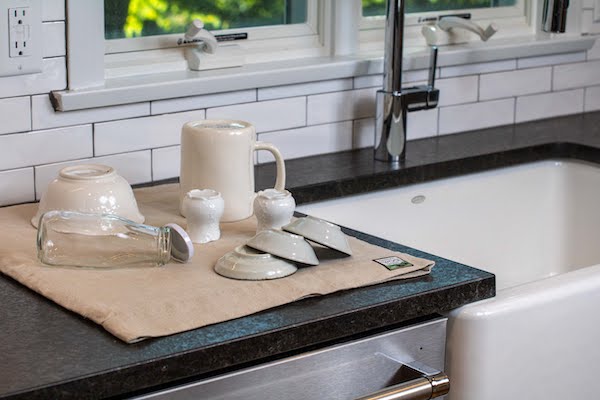 A beige drying drying mat with white dishes next to a white farm style sink