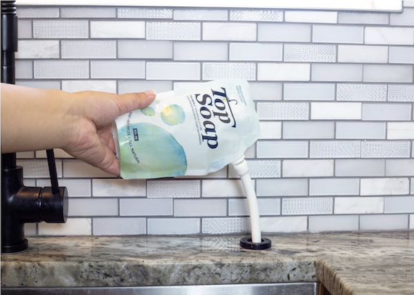A person's hand holding and pouring liquid soap into an in sink dispenser.
