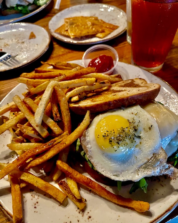 A plate with a fried egg topped sandwich and French Fries at Bacon Bros Public House Greenville SC