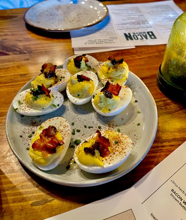 A platter of deviled eggs on a wood table with menus from Bacon Bros Public House Greenville SC