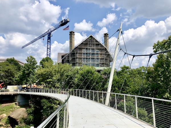 A suspension bridge through a park with a building under construction and a crane in Beautiful Greenville South Carolina
