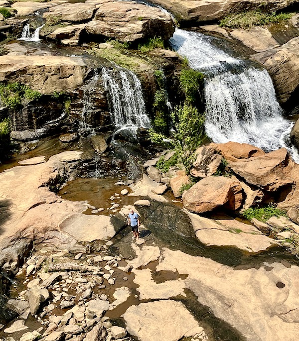 Seen from high above are rocks, waterfalls and a man in a blue T-shirt in Beautiful Greenville South Carolina