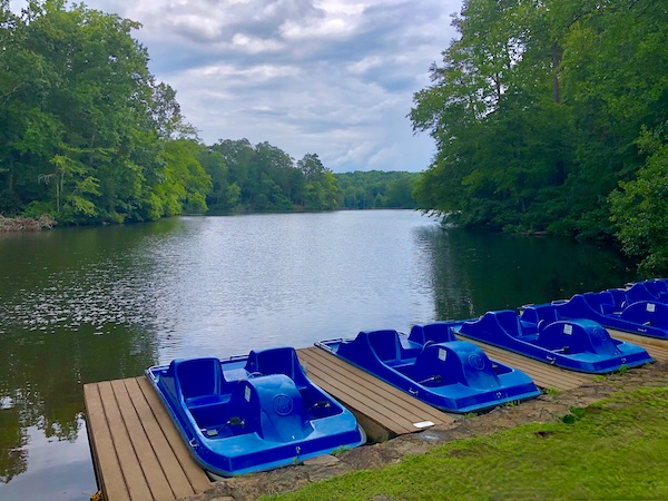 A large lake surrounded by trees and blue paddle boats docked in the foreground.
