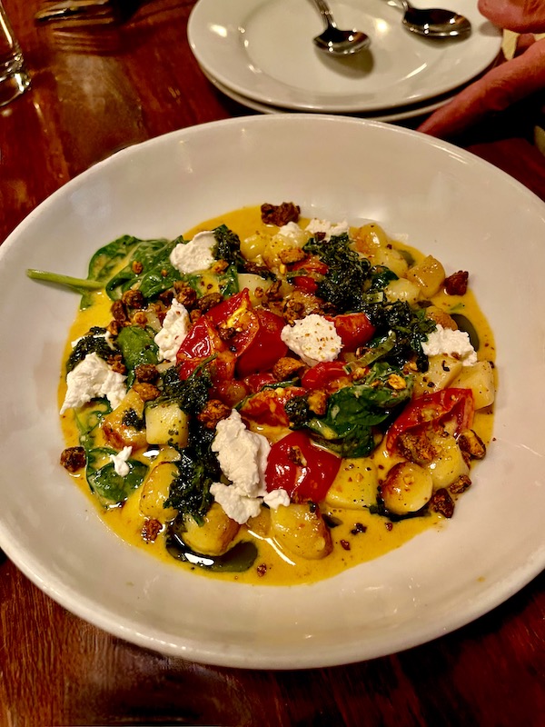 A large shallow ivory bowl filled with gnocchi, tomatoes, dollops of white goat cheese and spinach at Copper Crown Restaurant Asheville NC