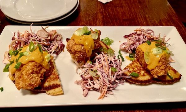 A rectangular white plate topped with a trio of fried chicken topped johnny cakes and a trio of slaw portions at Copper Crown Restaurant Asheville NC