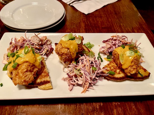 A rectangular white plate topped with a trio of fried chicken topped johnny cakes and a trio of slaw portions at Copper Crown Restaurant Asheville NC