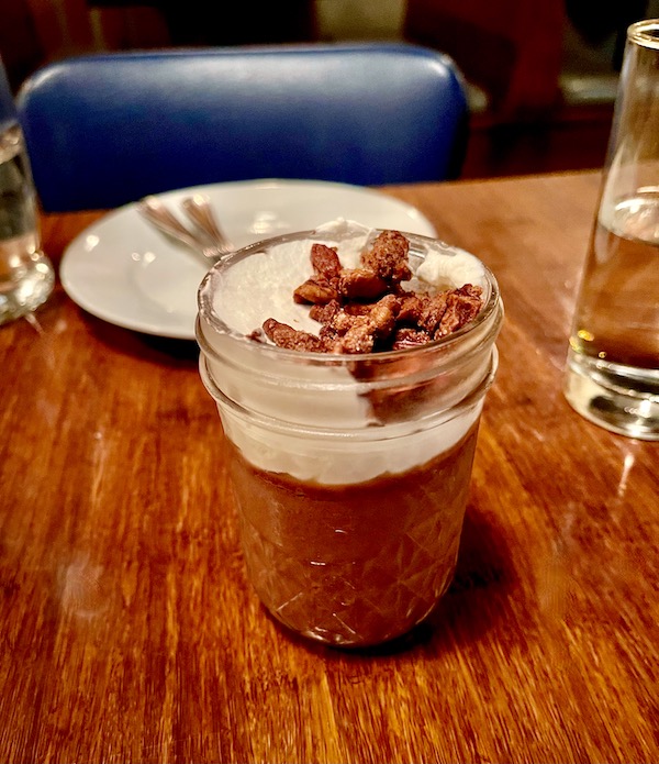 A jar of chocolate pudding topped with whipped cream and spiced nuts sitting on a wood tabletop at Copper Crown Restaurant Asheville NC