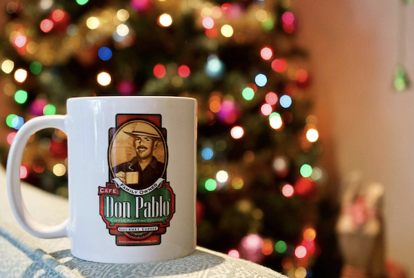 A white Don Pablo coffee mug in front of a decorated Christmas tree from 15 Best Gifts for Foodies and RVers