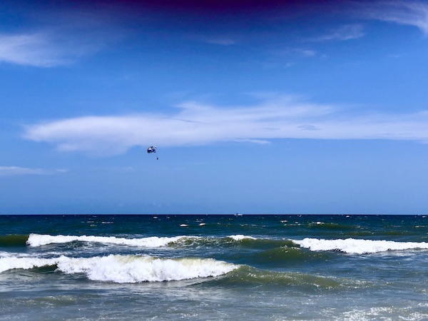 Ocean waves and a person hang gliding above them.