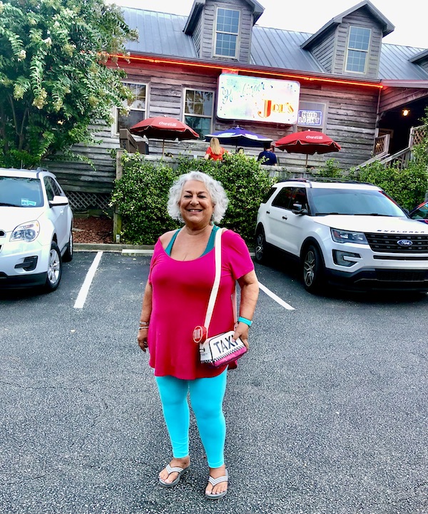 A silver haired woman in a pink top and blue pants in front of Hamburger Joe's North Myrtle Beach SC