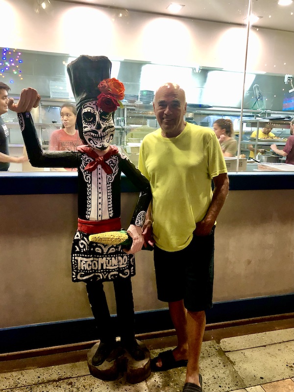 A man in a yellow T-shirt standing next to a statue of a Mexican "day of the dead" masked woman at Taco Mundo North Myrtle Beach