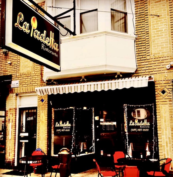 The outside of a restaurant with large black and gold sign, tables and red chairs at La Padella Ristorante Ventnor NJ