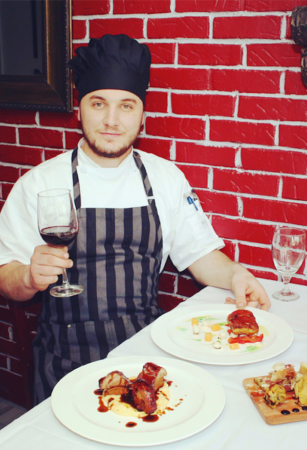 A chef with a black and white striped apron, holding a glass of red wine. A table with white cloth and plates of food at La Padella Ristorante Ventnor NJ