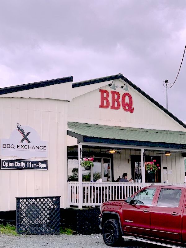 A large white building with a front porch and BBQ in bright red letters.