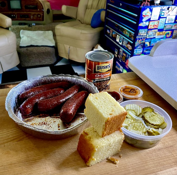 A wood board topped with sausages, cornbread, pickles, sauces and a can of beans from Louisa VA Small Town Big Impact