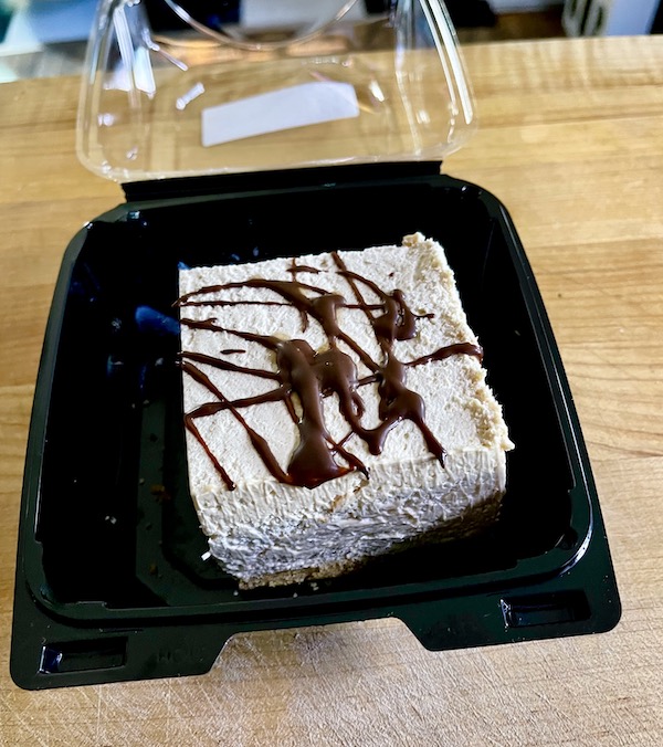 A black take-out clamshell with a square of peanut butter pie with chocolate drizzle.