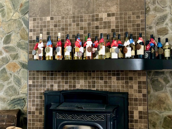 A stone wall fireplace with mantle holding wine awards