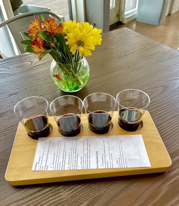 Four glasses of red wine on a wood tray and a vase of fresh flowers at 53rd Winery
