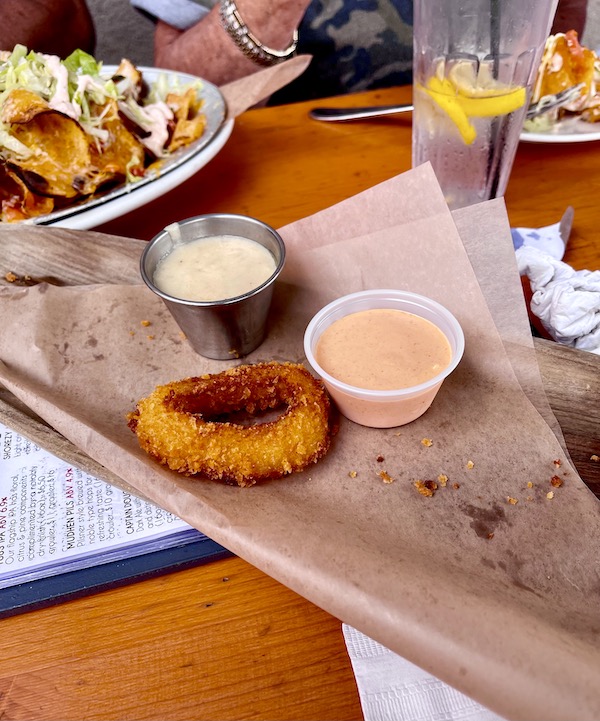A lone fried onion ring on a folded piece of brown paper and two sauces at Mudhen Brewing Wildwood NJ